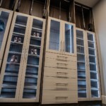 In this his and hers closet design, the cabinets for clothes and shoe racks have glass doors with wood frames.