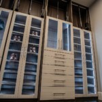 In this his and hers closet design, the cabinets for clothes and shoe racks have glass doors with wood frames.